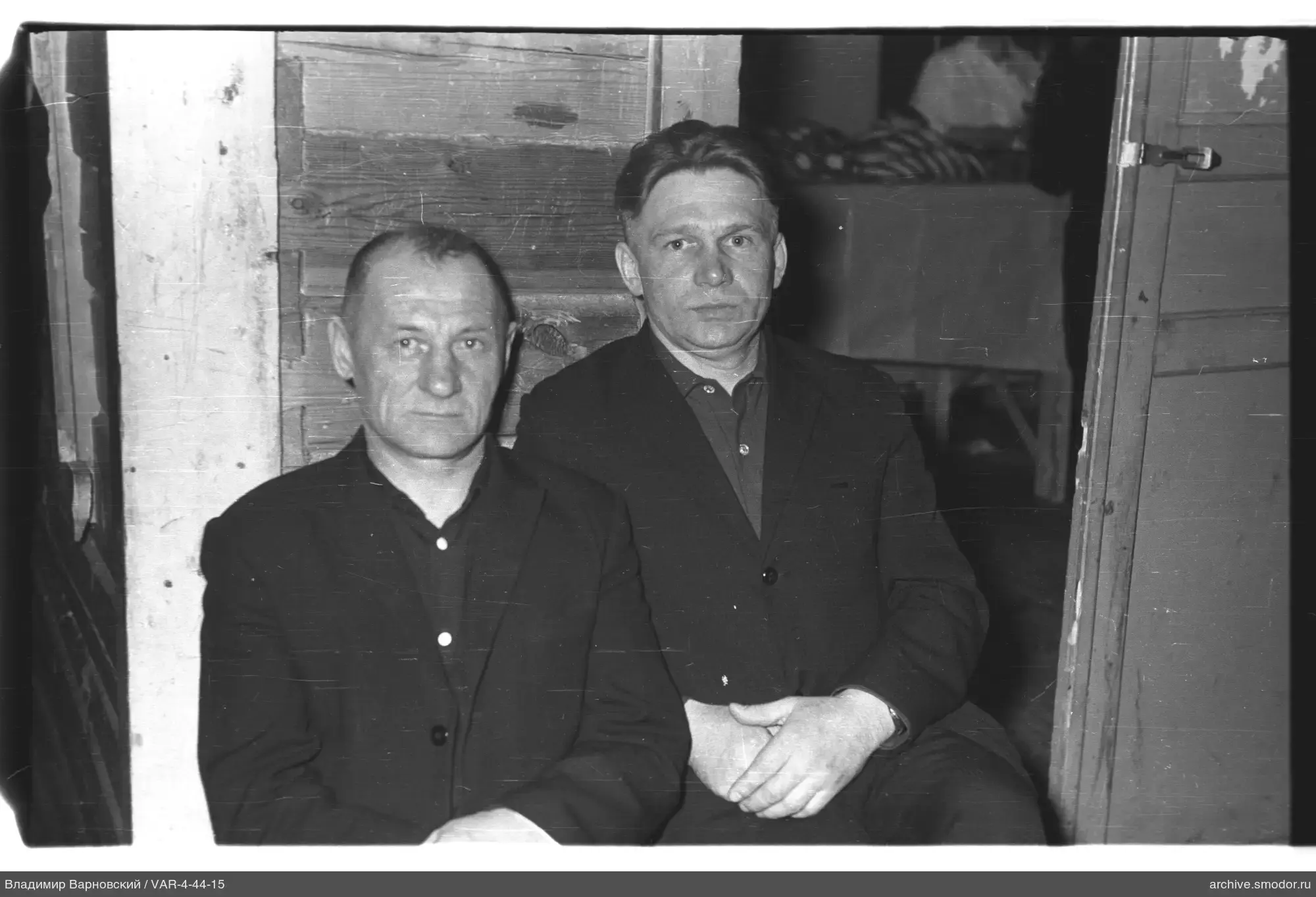 Two men sitting on a bench by a wooden wall