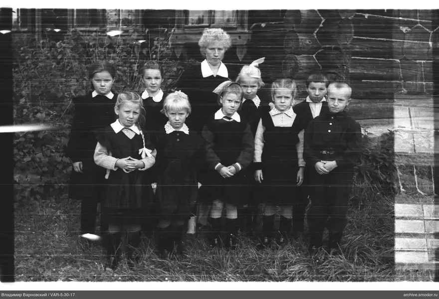 Gruppe von Kindern und Frau bei Holzgebäude