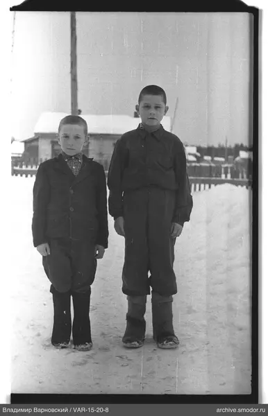 Zwei Jungen im Schnee vor einem Holzhaus