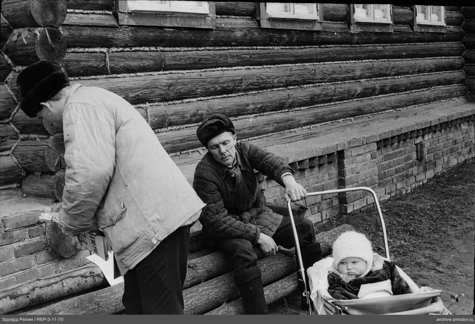 Männer mit Kinderwagen und Zeitung an Holzwand