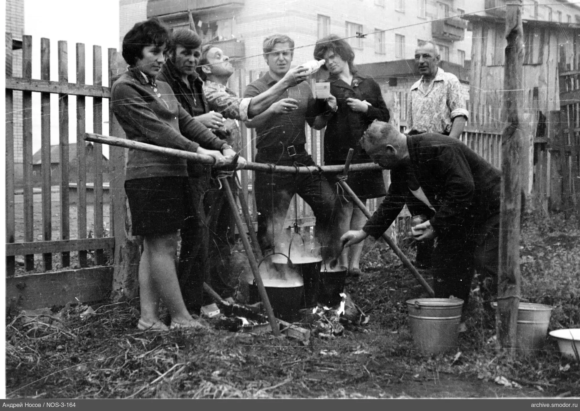 Gruppe um Lagerfeuer mit Kesseln und Holzzaun
