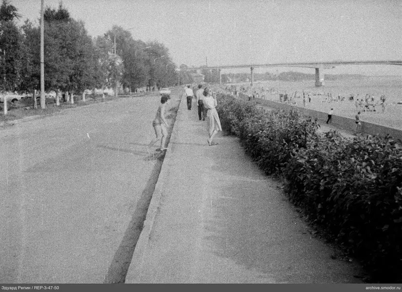 Menschen an der Uferpromenade mit Strand und Brücke
