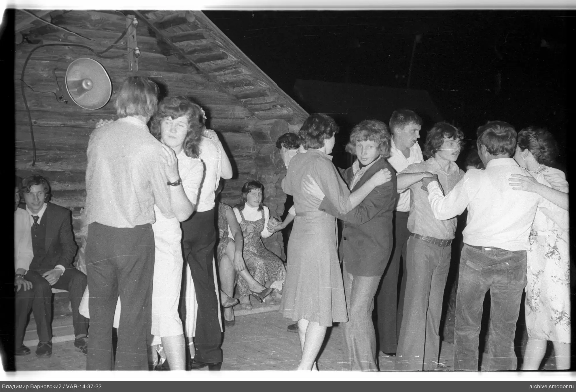 Couples dancing on an outdoor area near a wooden building