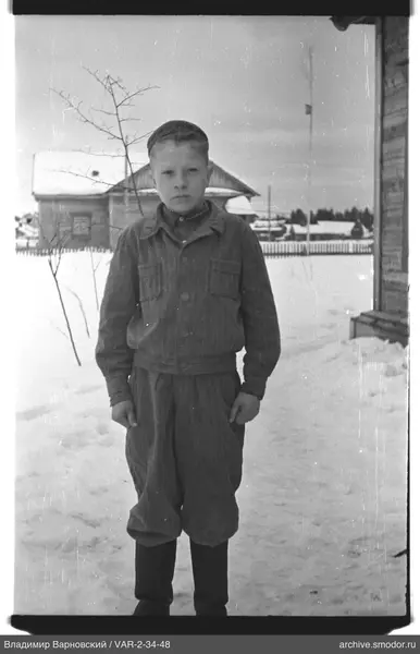 Junge im Schnee neben Holzhaus