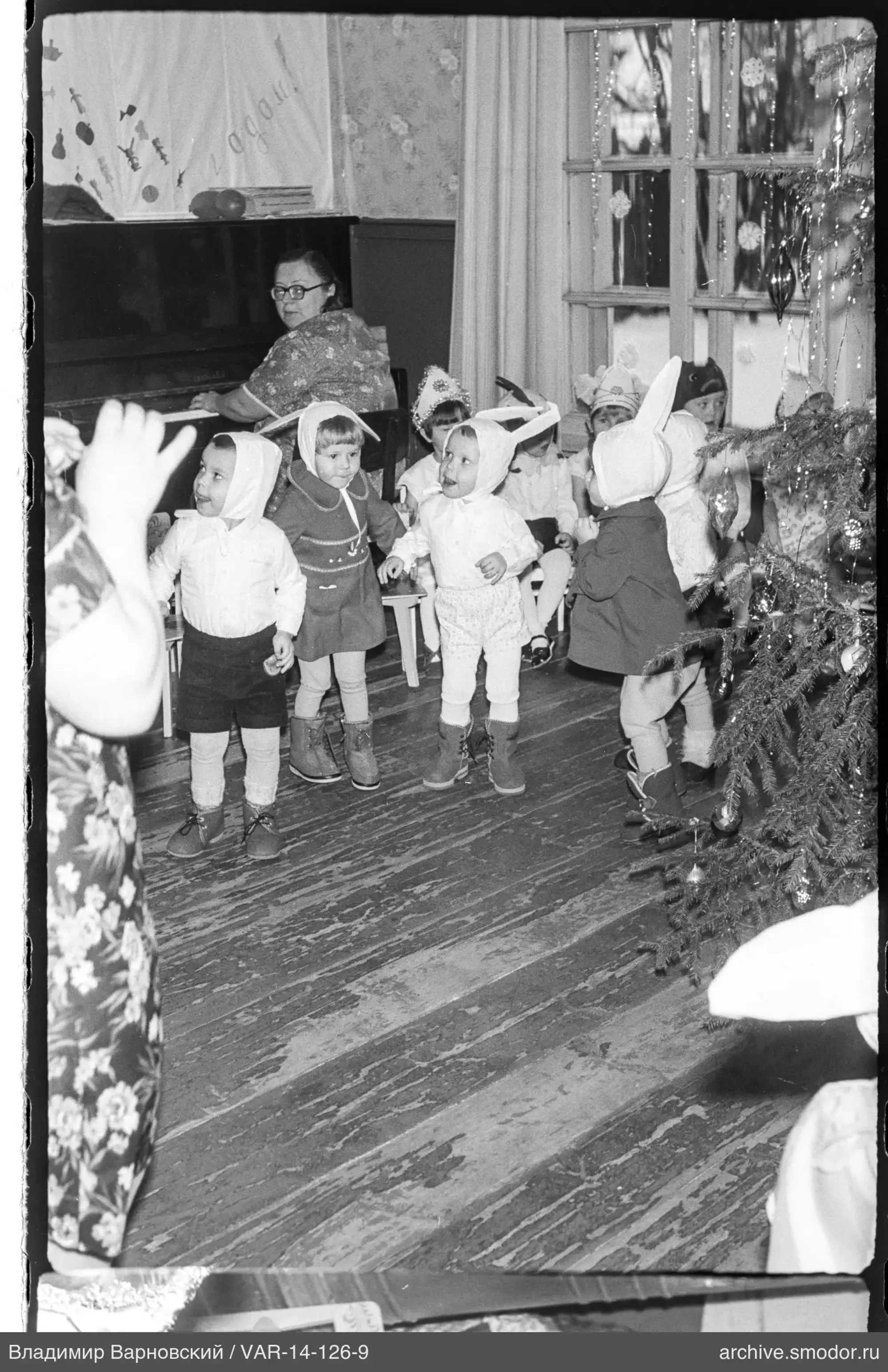 Kinder in Kostümen bei Weihnachtsbaum und Klavierspielerin