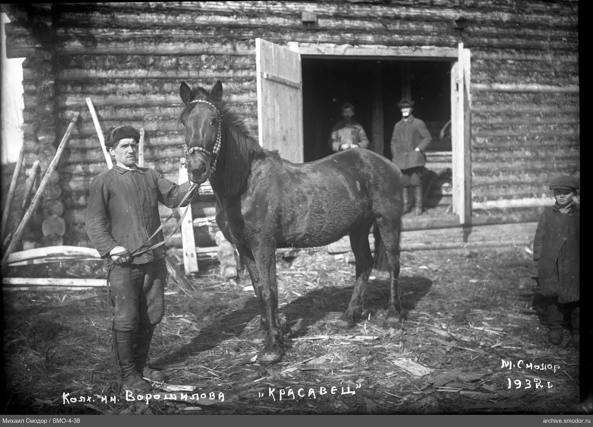 Mann mit Pferd vor Holzgebäude