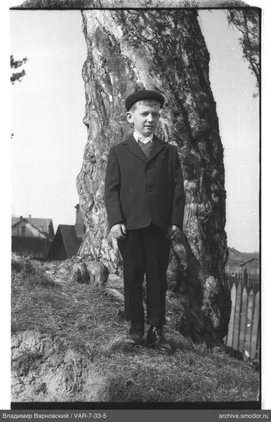 Junge in Anzug und Mütze neben Baum