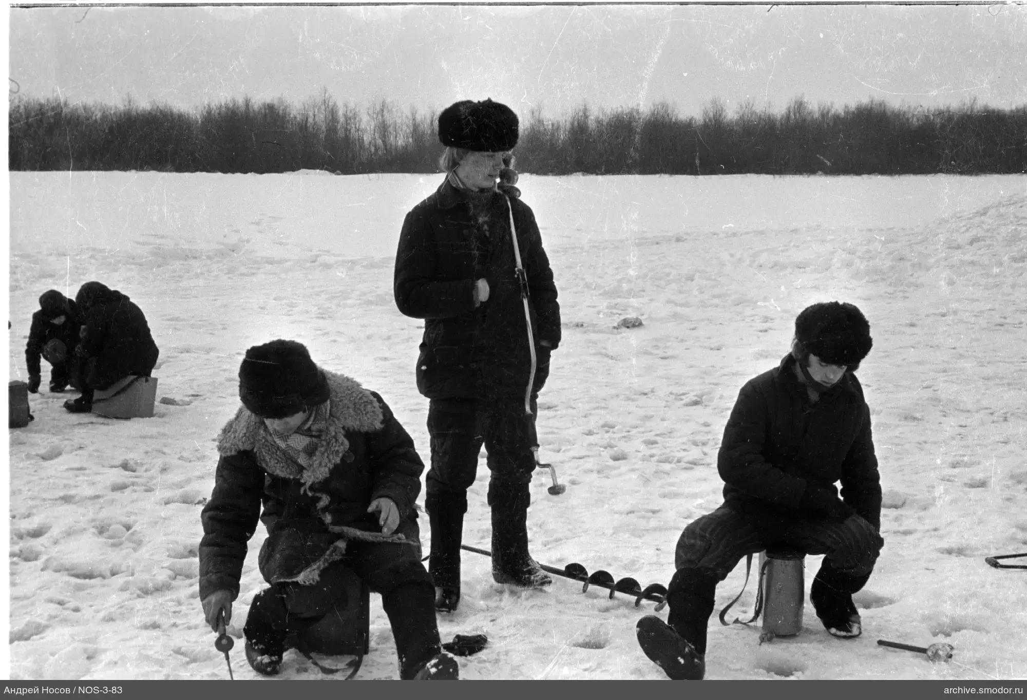Люди на заснеженной поверхности с ледобурами