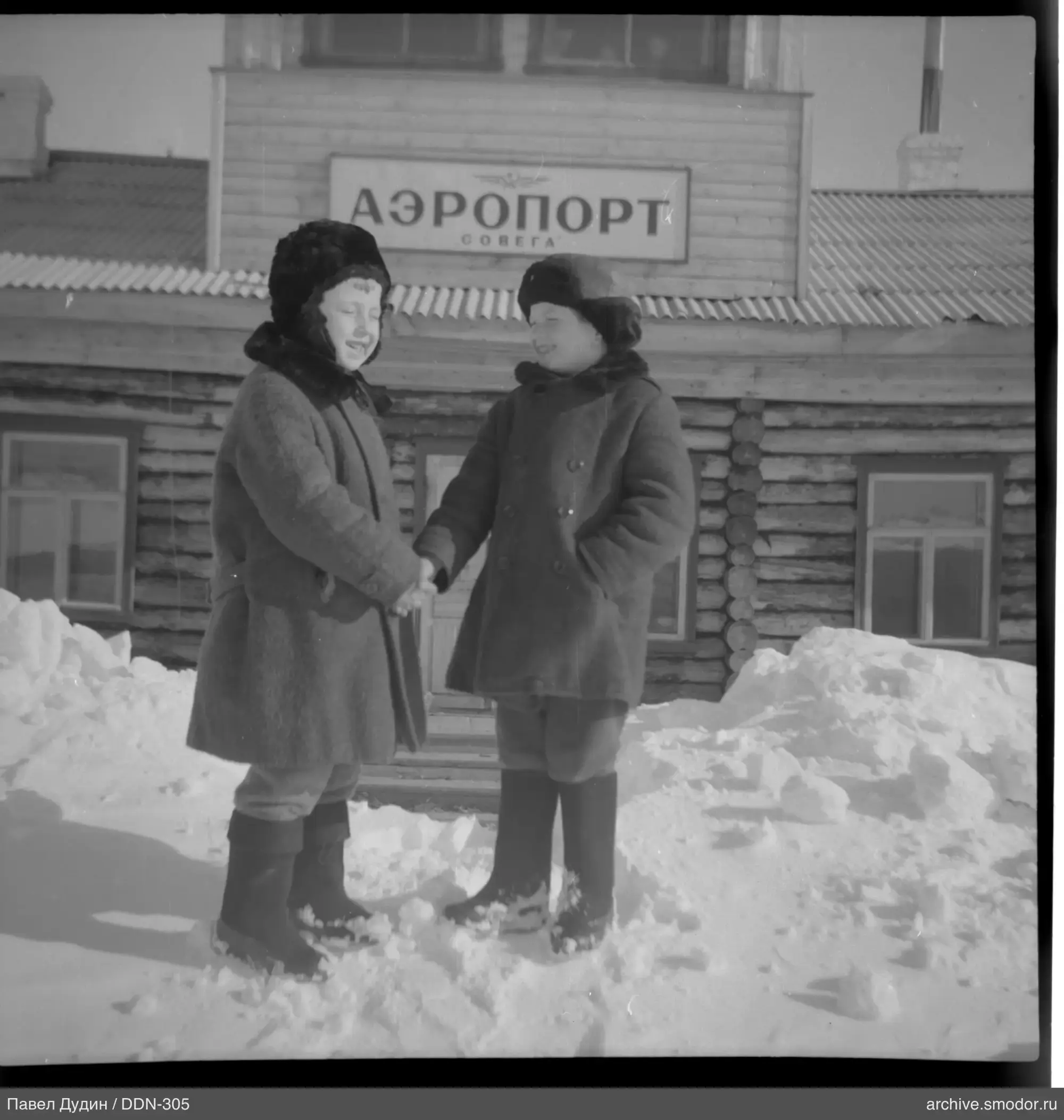 Два ребёнка у деревянного здания с вывеской "АЭРОПОРТ СОВЕГА"