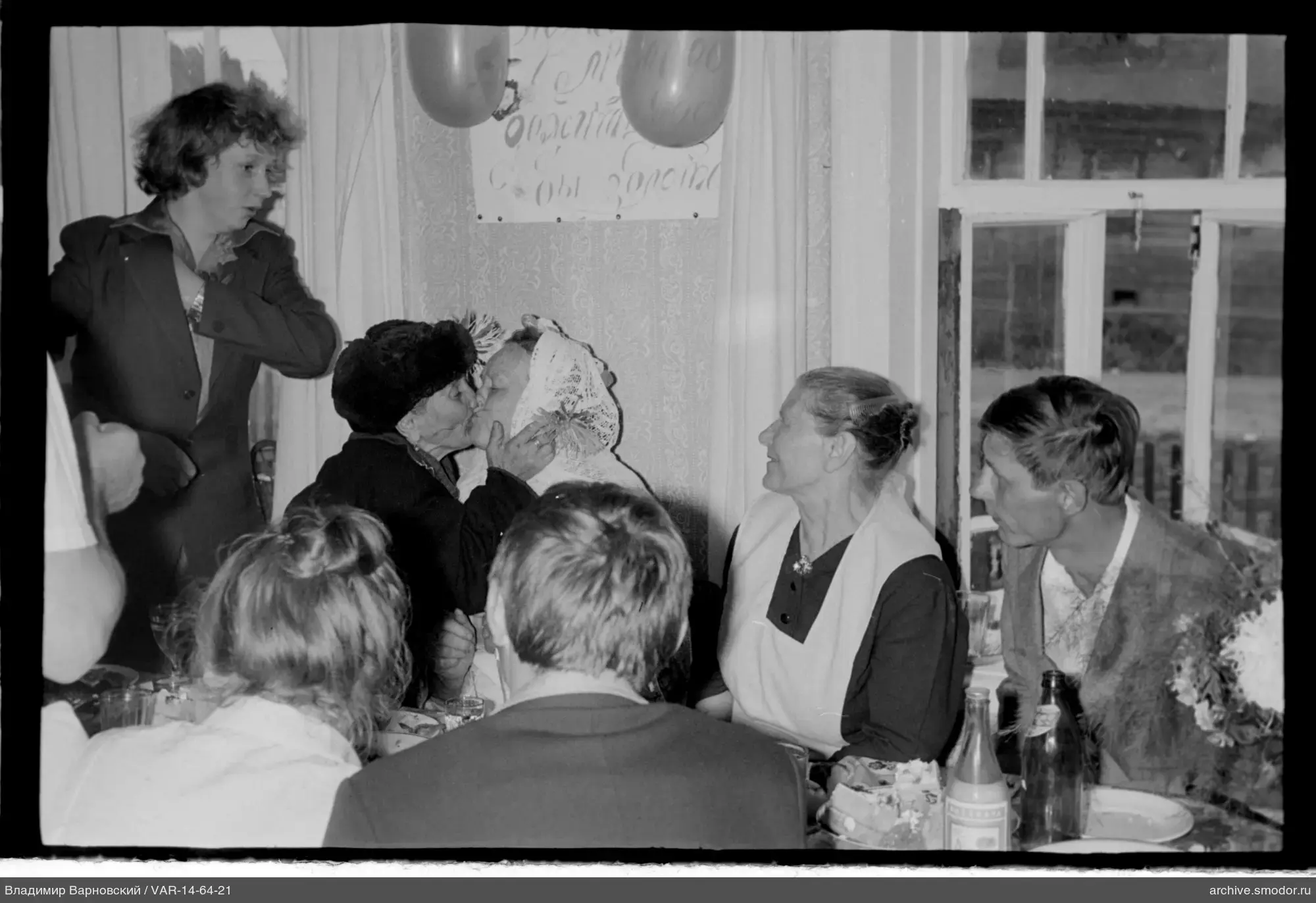 Menschen am Tisch, ältere Frauen küssen sich