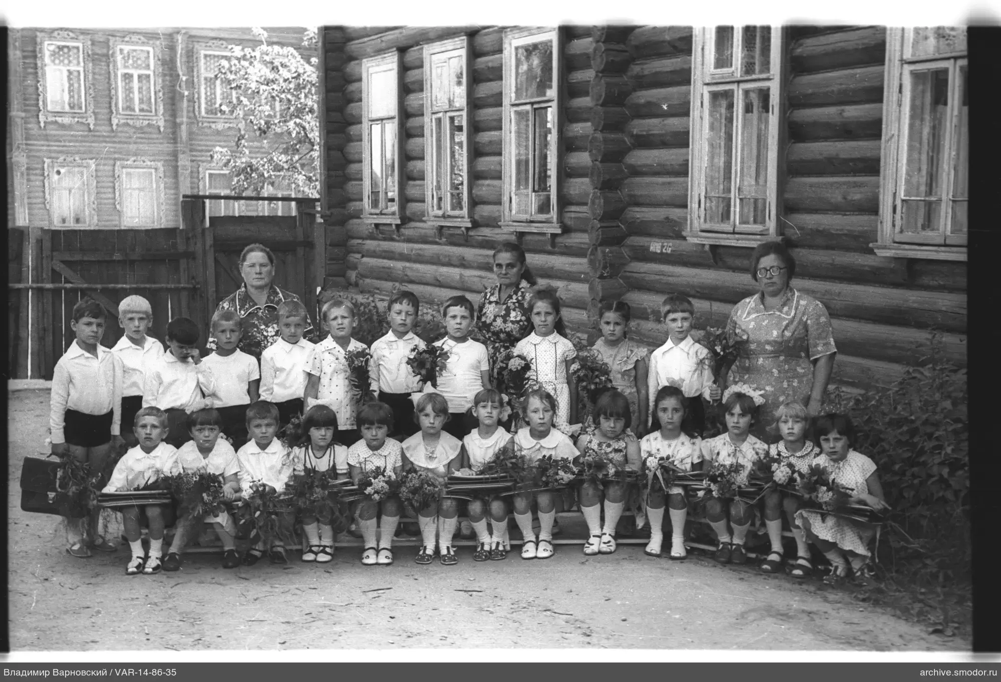 Gruppenporträt von Kindern und Frauen bei einem Holzhaus