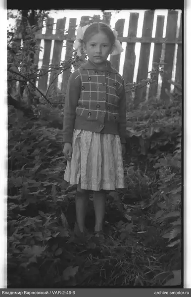 Mädchen in Strickjacke und Rock am Zaun