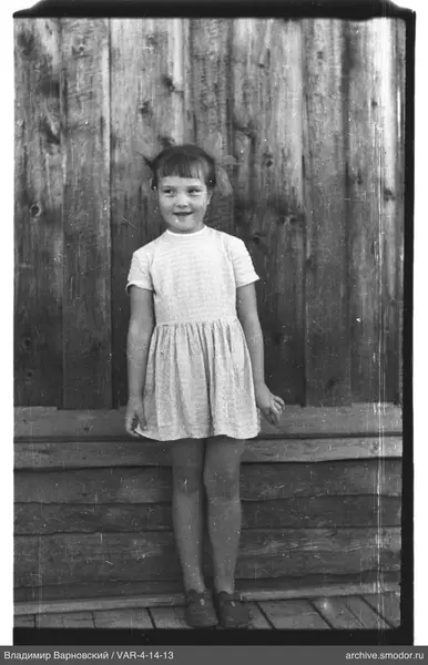 Mädchen in hellem Kleid vor Holzwand