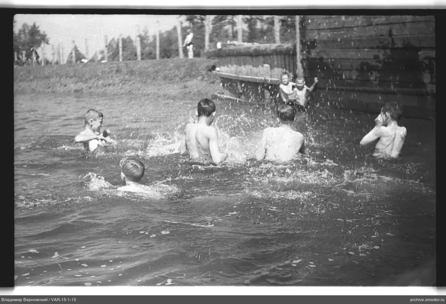 Kinder im Wasser und am Ufer bei einem Holzgebäude
