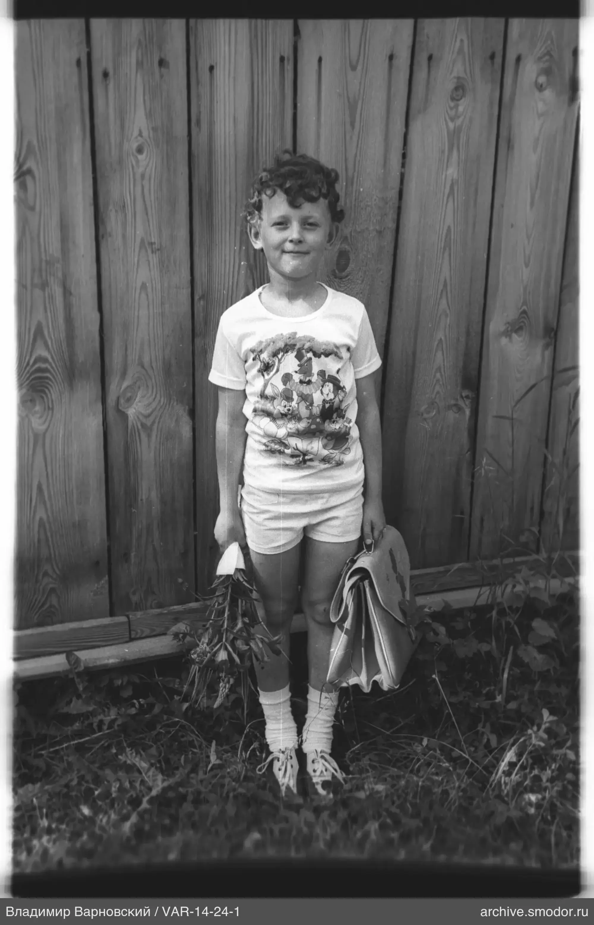 Junge mit Blumenstrauß und Schultasche am Zaun