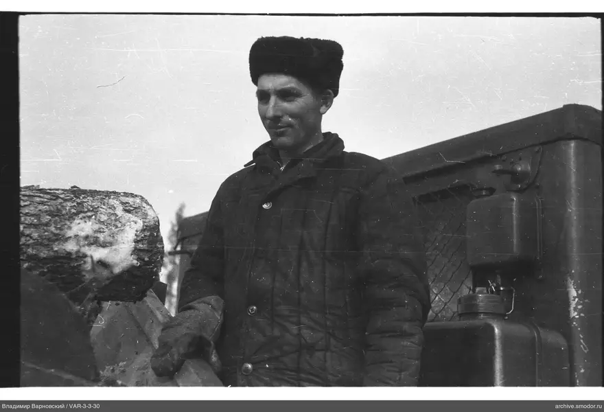 Man in quilted jacket and fur hat by log