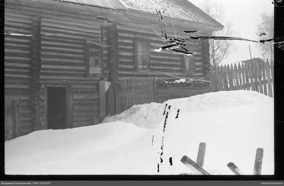 Holzblockhaus mit Schneehaufen und Zaun