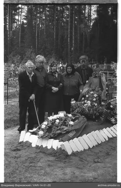Gruppe bei Grab mit Blumenkränzen