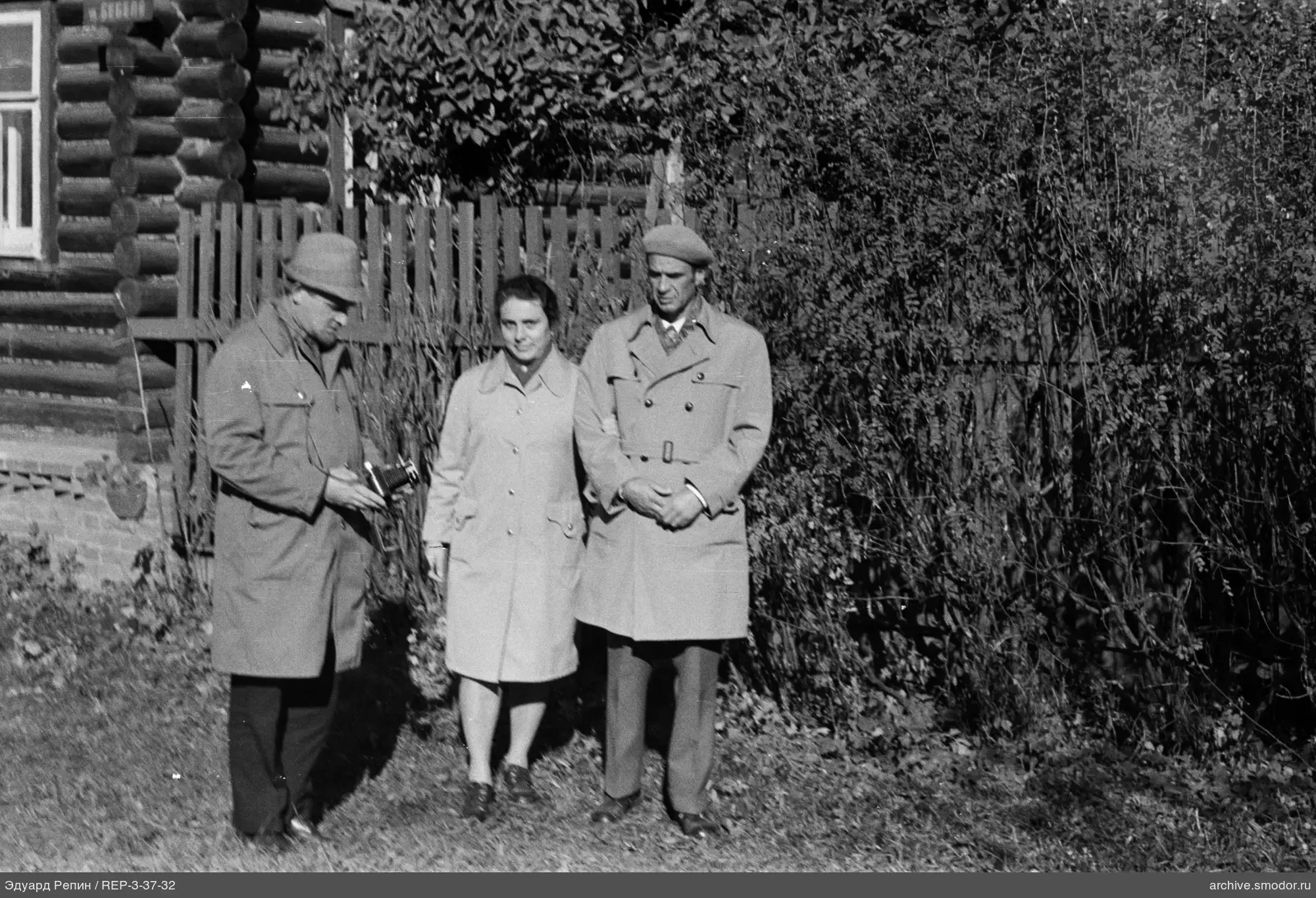 Gruppe von drei Personen bei einem Holzhaus