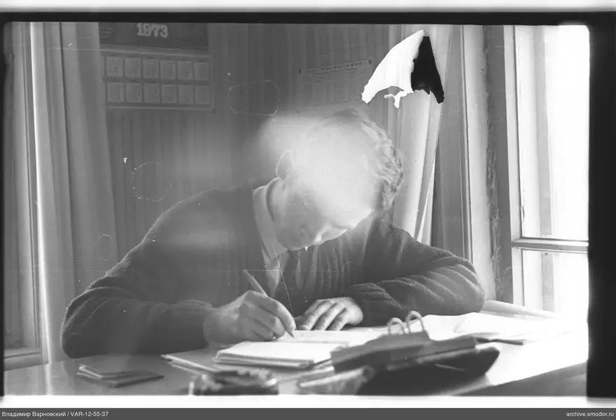 Man writing at a table by the window