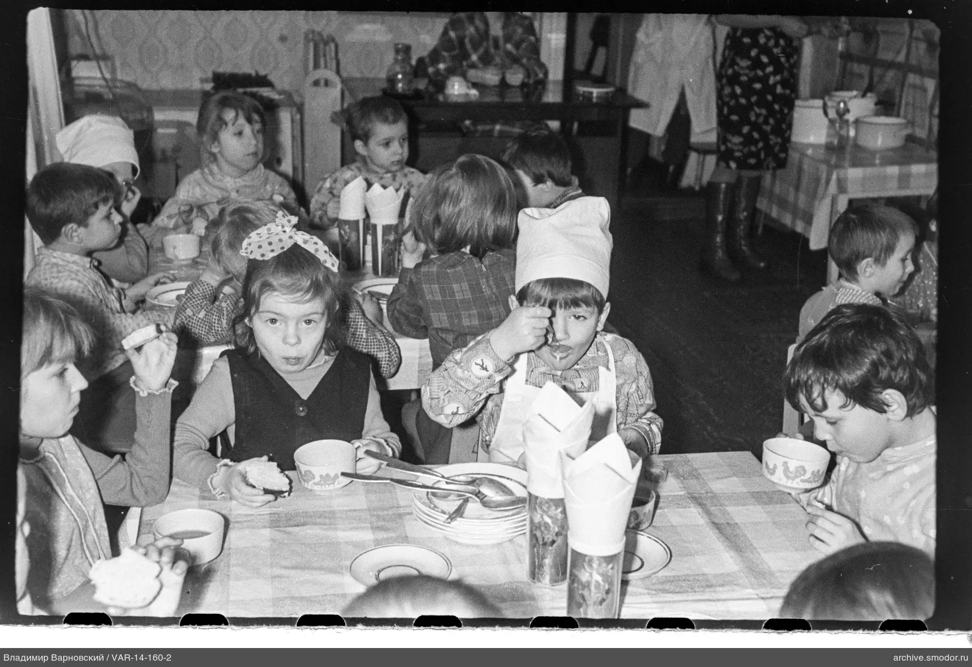 Kinder an Tischen mit Essen und eine erwachsene Frau
