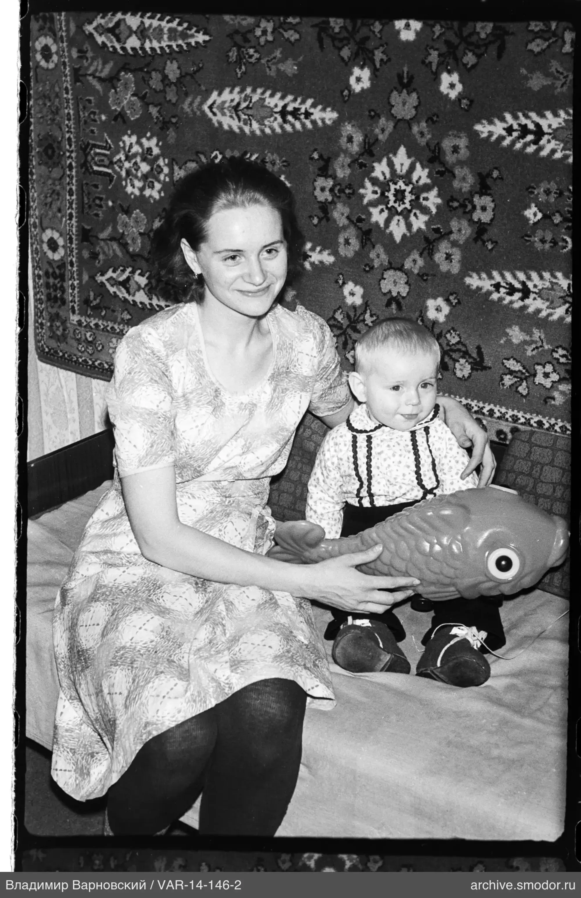 Женщина с игрушкой рыбы и ребёнок на диване