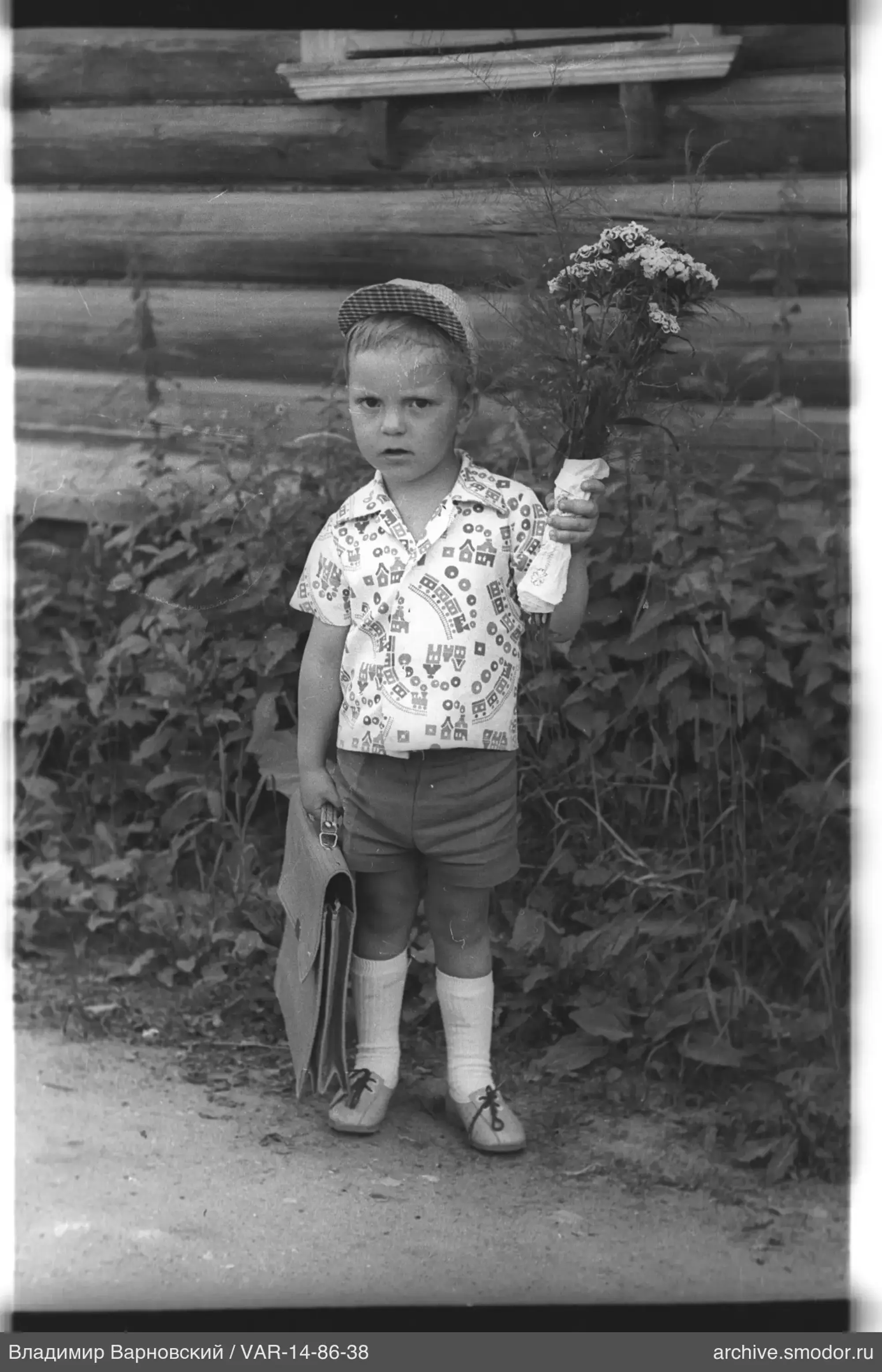 Kind mit Blumenstrauß und Schultasche bei Haus