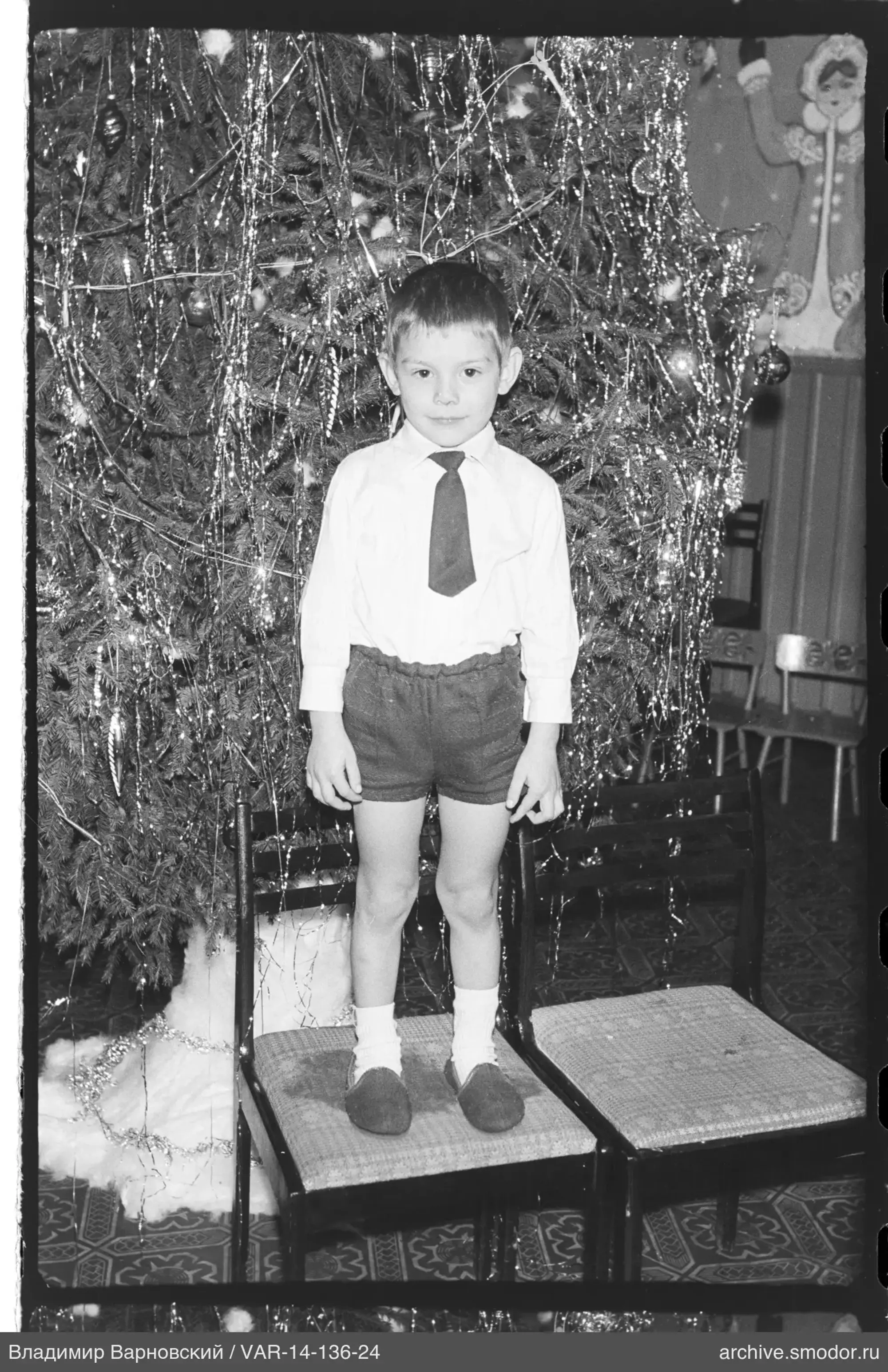 Boy standing on chairs in front of Christmas tree