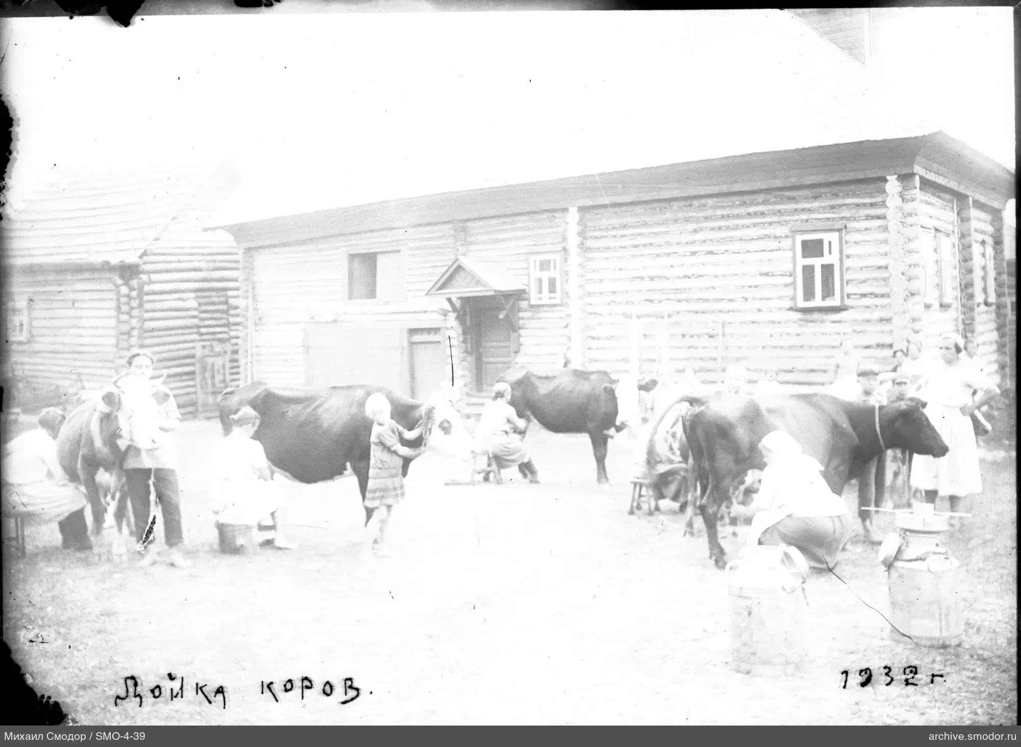 Frauen und Kinder melken Kühe vor Holzhaus