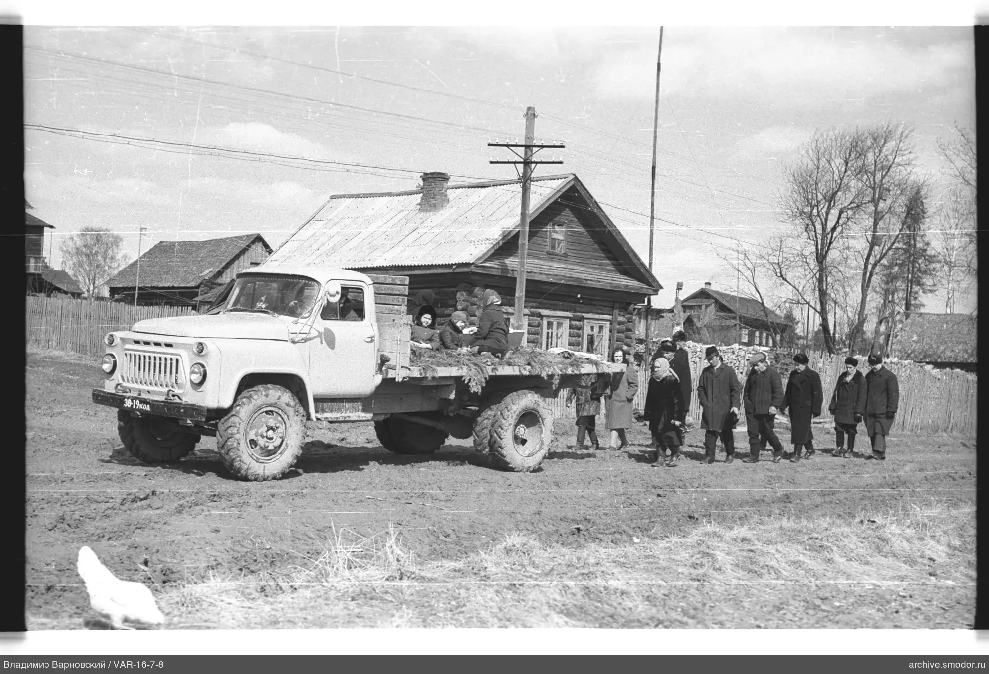 White truck with women and children near wooden house
