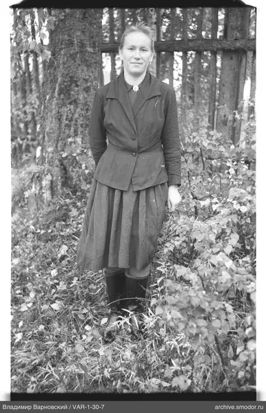 Женщина в пальто и юбке у забора