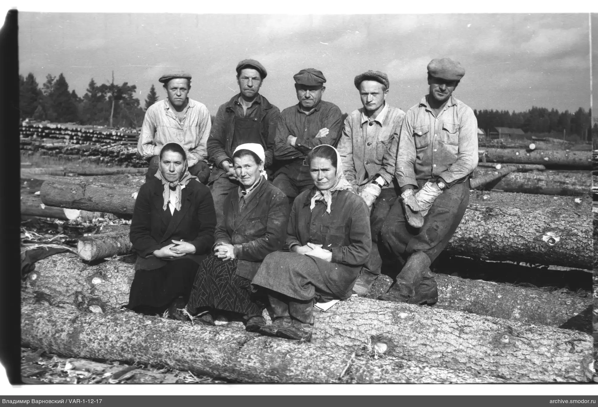 Gruppe auf Baumstämmen vor Wald und Gebäuden