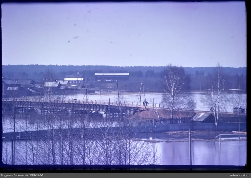 Wooden bridge with two people and houses