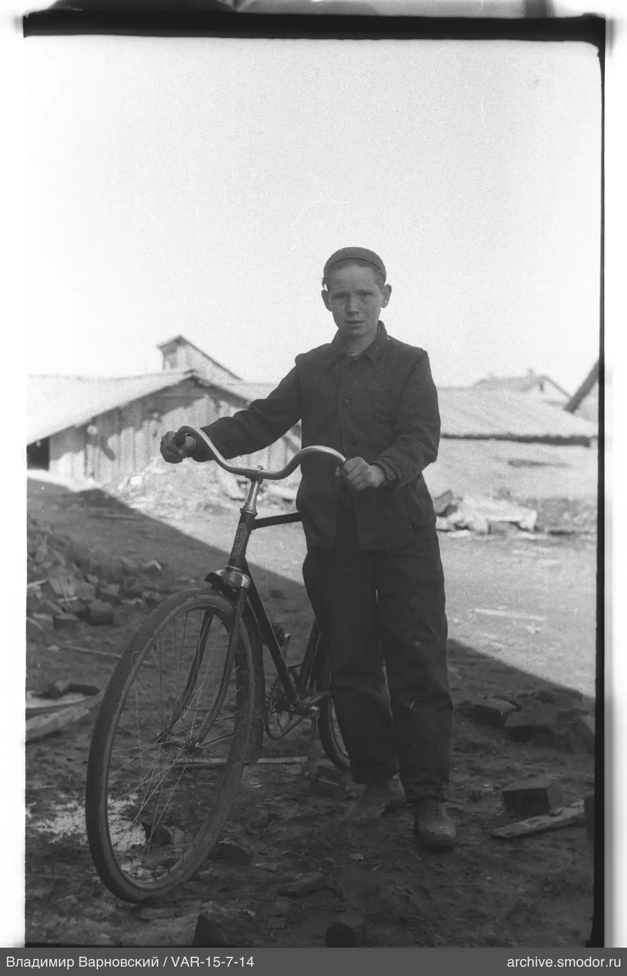 Junge mit Fahrrad vor Holzhäusern