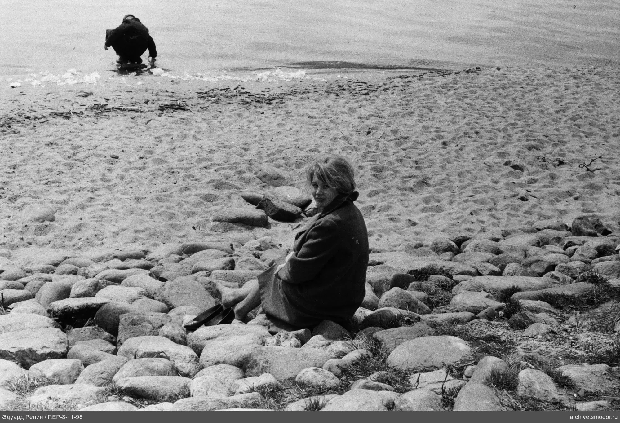 Frau am Ufer mit Schuhen und Person im Wasser