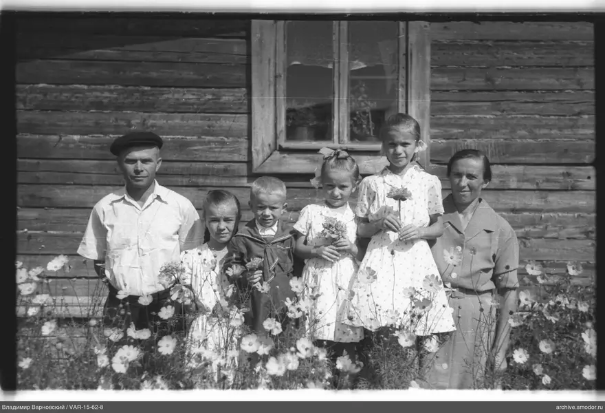 Gruppe von Erwachsenen und Kindern vor einem Holzhaus