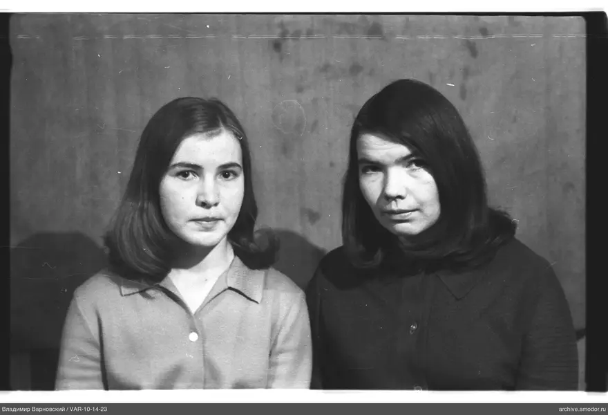 Two women sitting against a plain wall