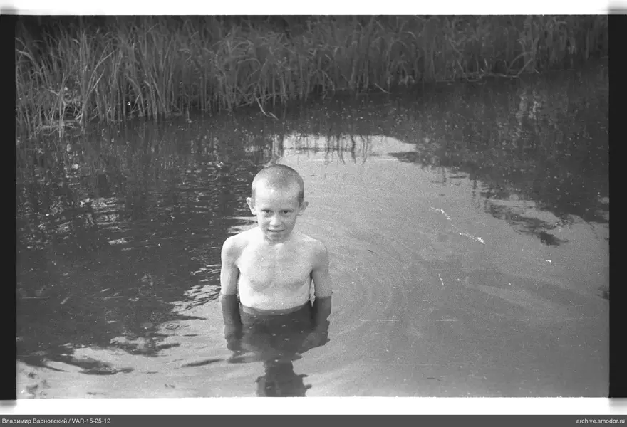 Junge im Wasser vor hohem Gras