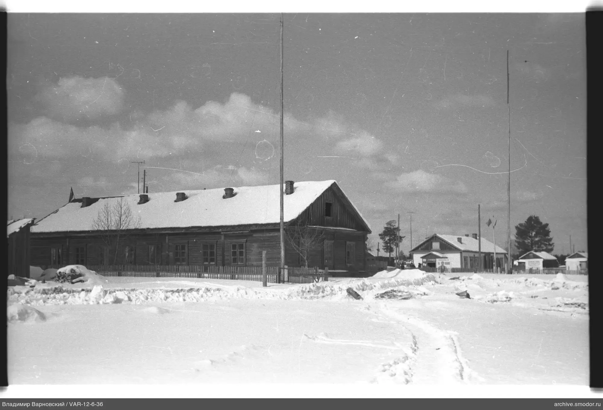 Zwei Holzhäuser mit Schnee und Fahnenmasten