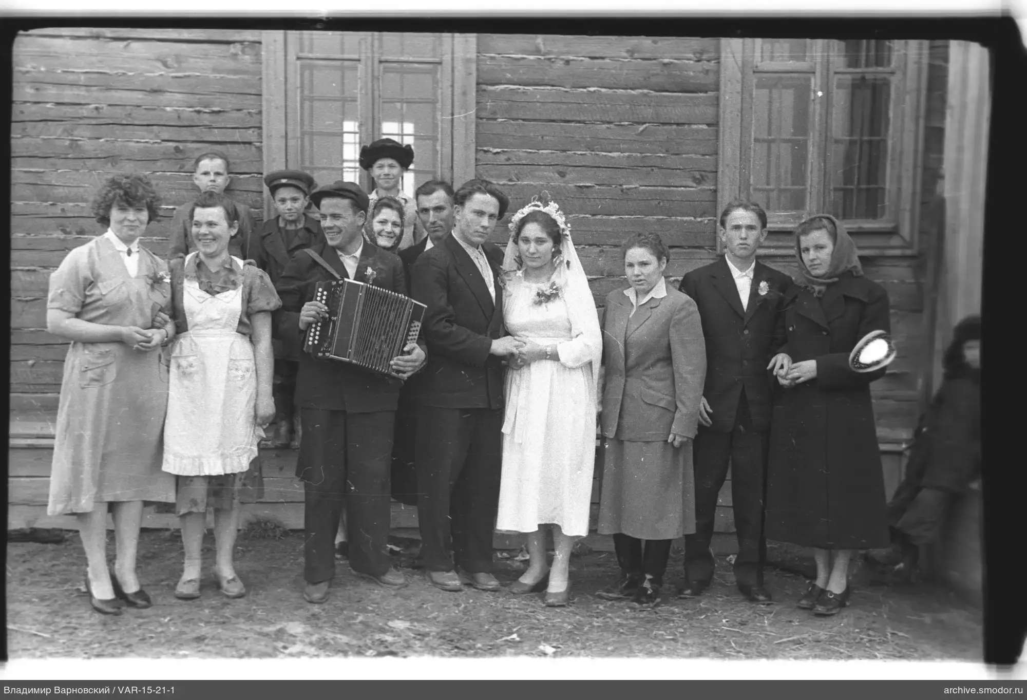 Hochzeitspaar mit Gästen vor einem Holzhaus