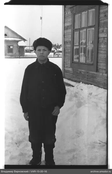 Junge im Schnee neben Holzhaus