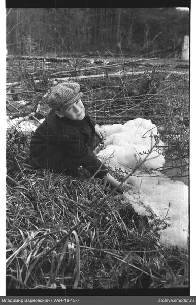 Junge in dunklem Mantel und Kappe auf Gras