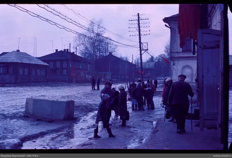 Children and adults on muddy street with flags