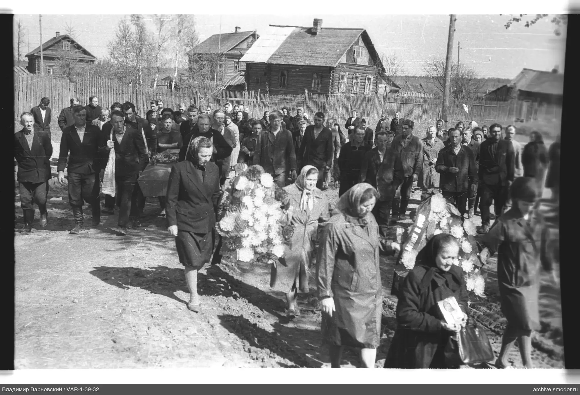 Группа людей на сельской дороге с венками и фотографией