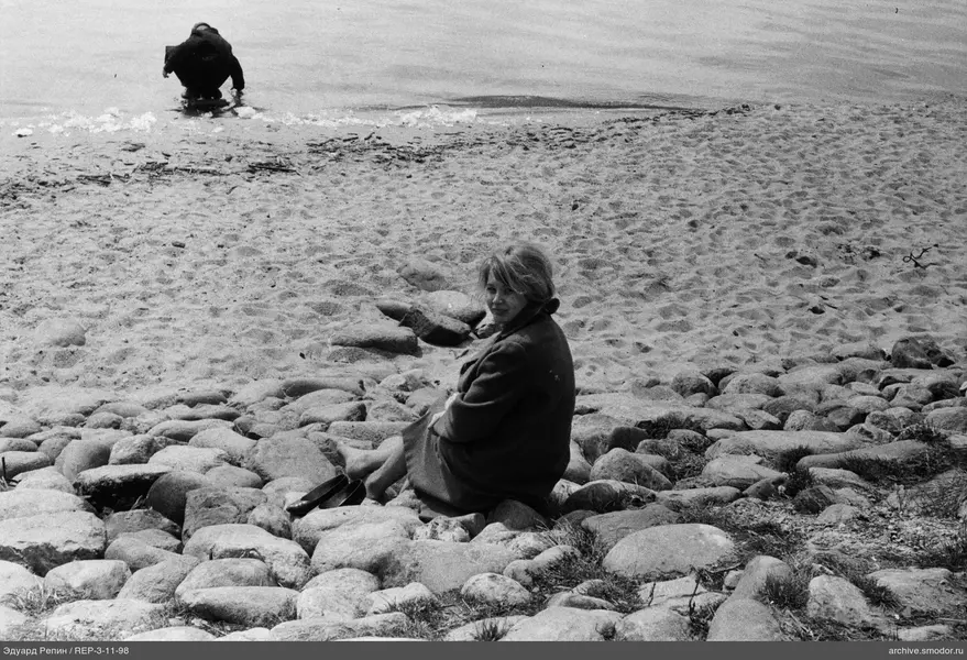 Frau am Ufer mit Schuhen und Person im Wasser